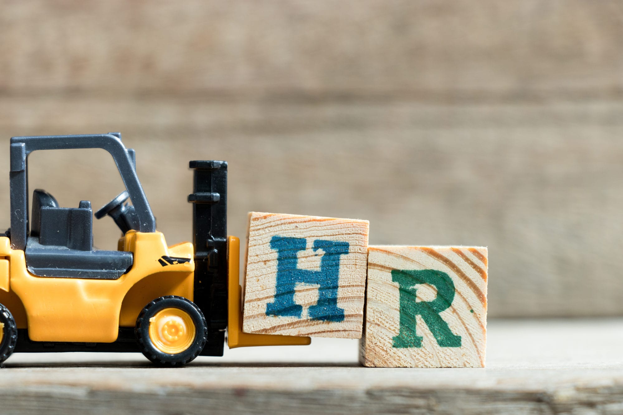 Toy yellow forklift hold letter block H to complete word HR (Abbreviation of Human resource)on wood background Toy yellow forklift hold letter block H to complete word HR (Abbreviation of Human resource)on wood background