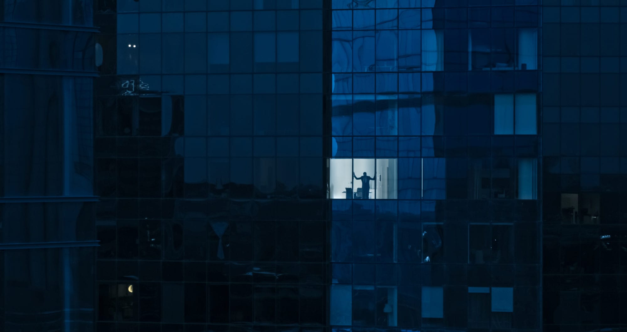 Aerial Shot: From Outside into Office Building with Businessman Looking out of the Window. Shot of The Financial Business District Skyscrapers in the Evening. Aerial Shot: From Outside into Office Building with Businessman Looking out of the Window. Shot of The Financial Business District Skyscrapers in the Evening.